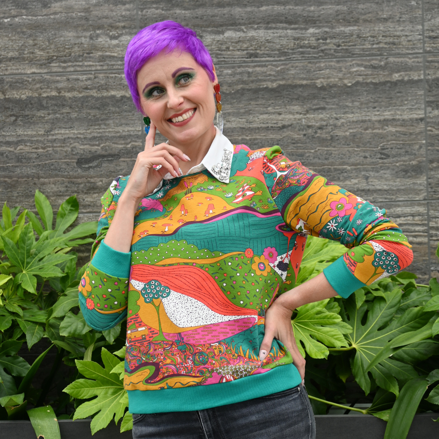 Model with purple pixie hair wearing the Blue Platypus Landscape Pullover in Emerald layered over a white collared shirt.