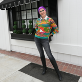 Full-length outdoor street-style view of a model wearing the Blue Platypus Landscape Pullover in Emerald with black jeans and knee-high boots.