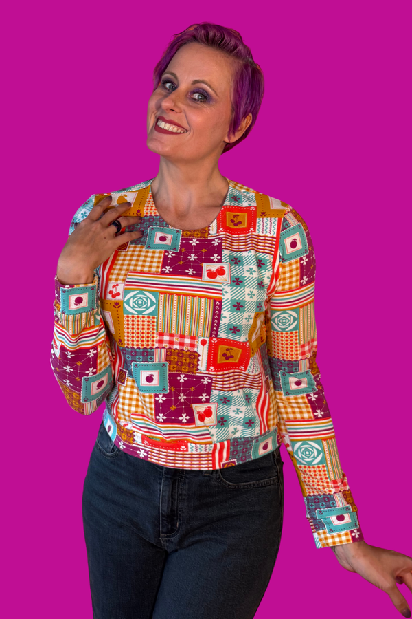 Front view portrait of a model with short purple hair wearing the Blue Platypus Patchwork Pullover in Magenta against a bright pink background.
