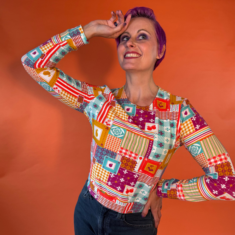 Model posing dynamically in dark jeans and the Blue Platypus Patchwork Pullover in Magenta showcasing the long sleeves.
