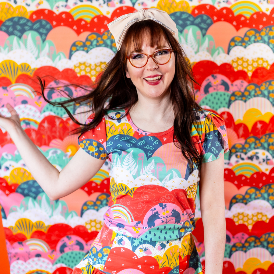 Model in hair bow and glasses posing dynamically while showcasing the tulip sleeves and raccoons and strawberry print on the Blue Platypus top.