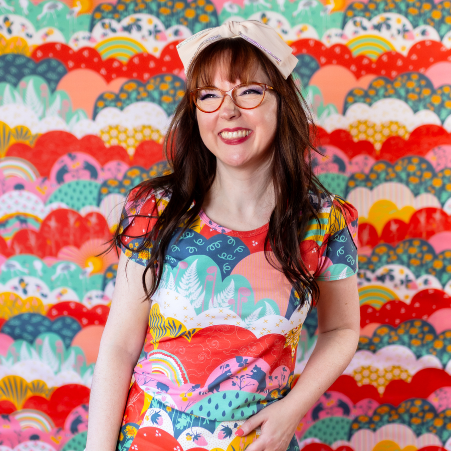 Studio portrait of a smiling woman with glasses wearing the Blue Platypus Tulip Sleeve Top in Mint & Strawberry Meadow Print against a colorful background.