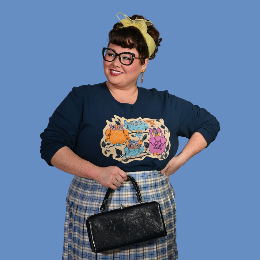 Close-up shot of a model with dark hair wearing the Blue Platypus Wacky Owls Pullover in Midnight Blue displaying the mod owl graphic.