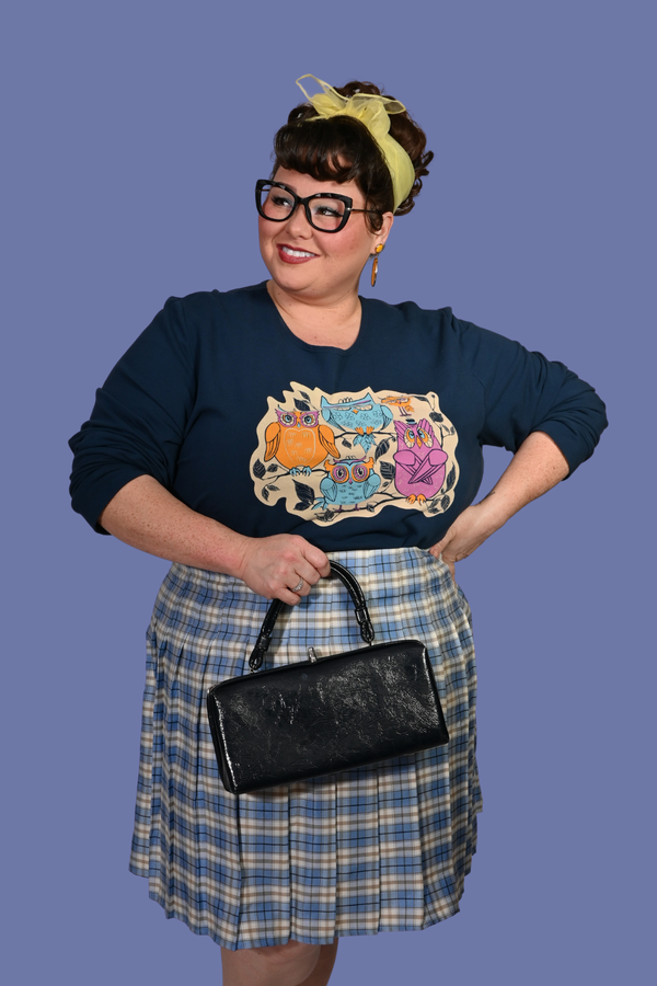 Plus-size model with cat-eye glasses wearing the size-inclusive Blue Platypus Wacky Owls Pullover tucked into a blue plaid skirt.