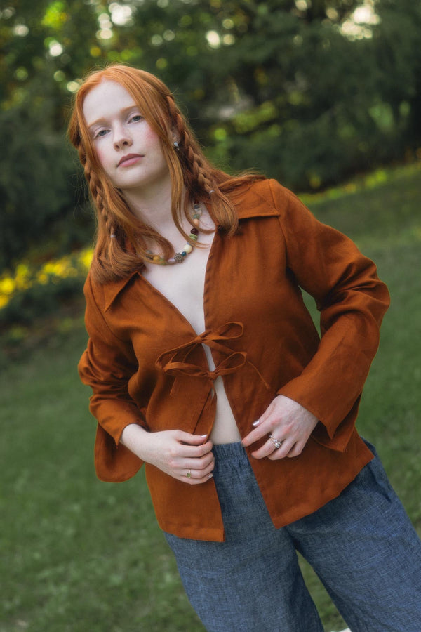 Model Bronwyn wearing the 100% linen Conscious Clothing Cirrus Top in Rust with front tie details outdoors in a natural park setting.