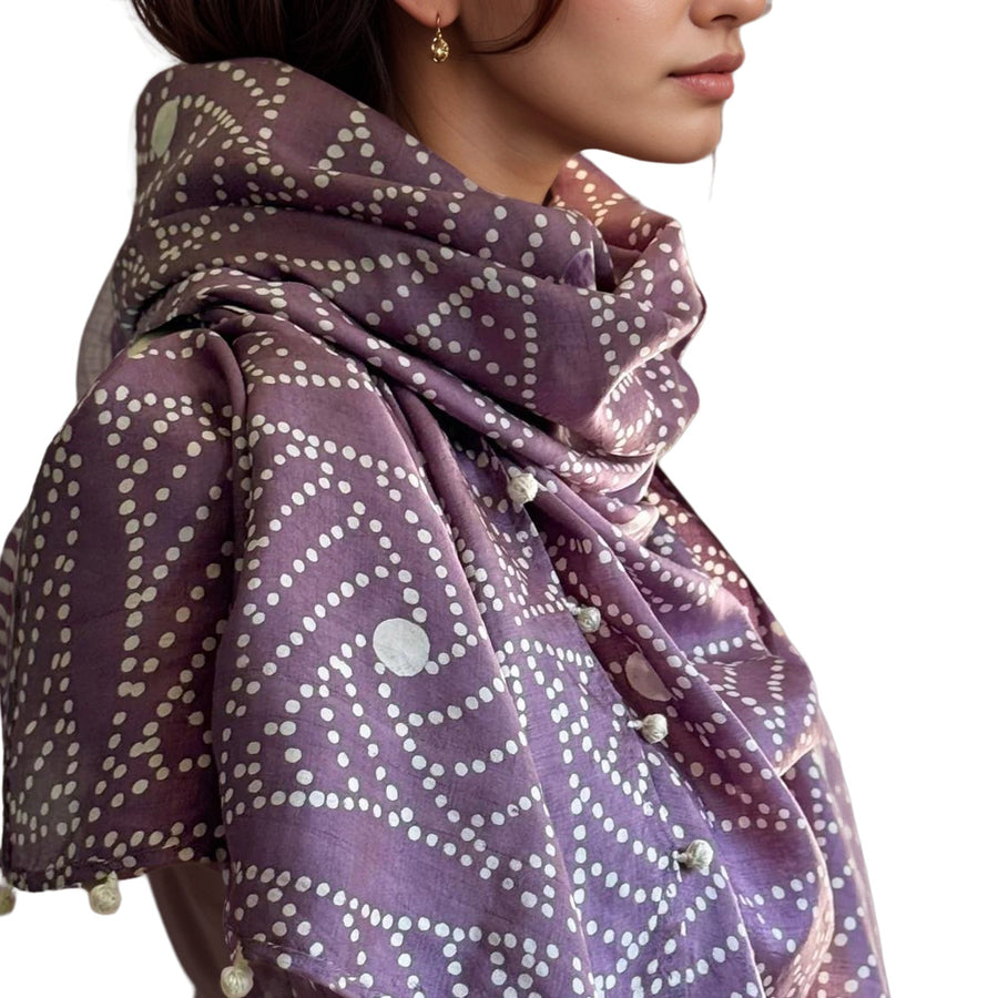 Side profile shot of a model wearing the luxurious Fyoli Fyoli DEWBERRY silk scarf wrapped softly around her neck, highlighting the rich purple hue, geometric white block-printed dots, and a glimpse of an elegant gold hoop earring.