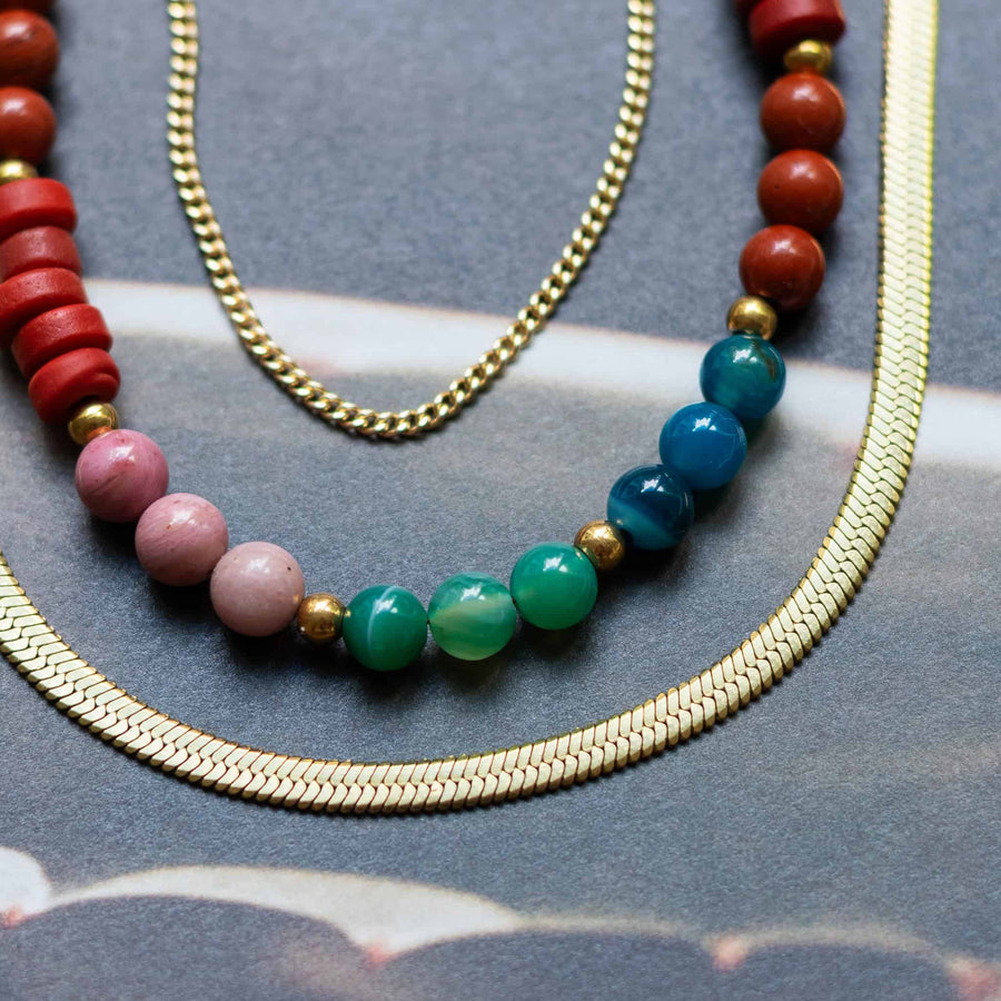 Close-up shot of the Phoebe Gemstone Necklace layered with a gold herringbone chain and curb chain.