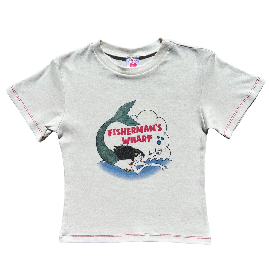 Front flat lay view of the Fruit Face Hard to Catch Off-White Baby Tee featuring a Fisherman's Wharf mermaid graphic and red contrast stitching.