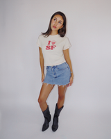 Full-length view of a model styled in the Fruit Face I Heart SF Baby Tee, denim mini skirt, and black cowboy boots.