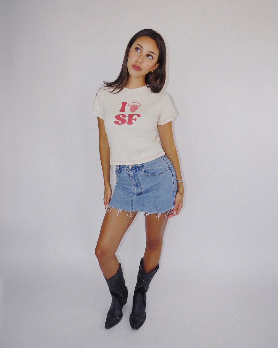 Full-length view of a model styled in the Fruit Face I Heart SF Baby Tee, denim mini skirt, and black cowboy boots.