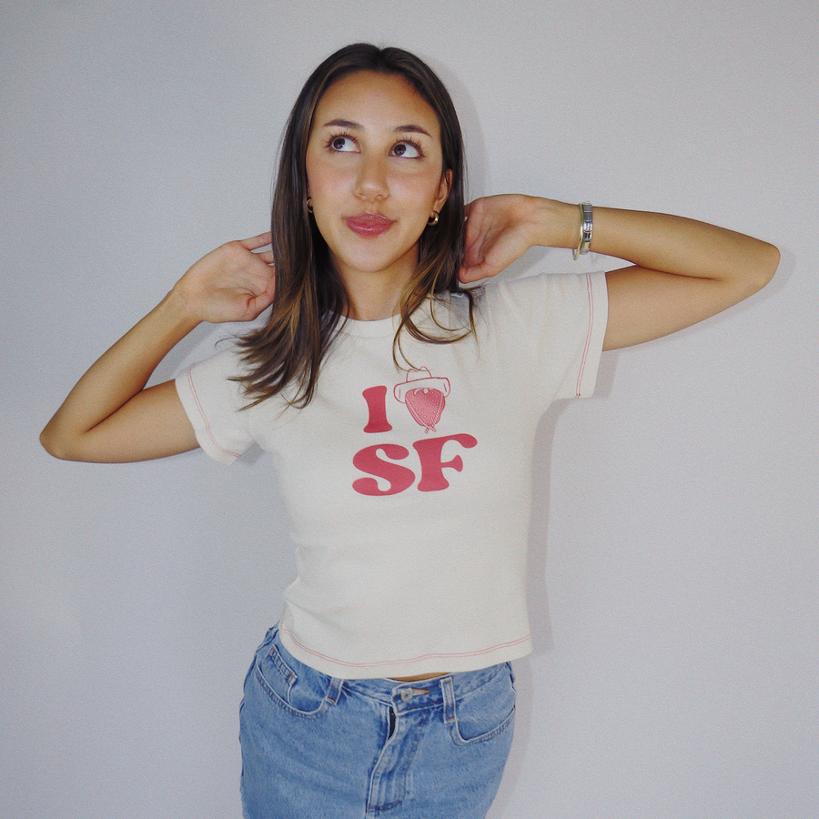 Studio portrait of a model looking up while wearing the off-white Fruit Face I Heart SF Baby Tee with red stitching.