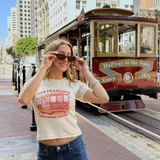 Model Alec wearing the Fruit Face Just Passing Through Baby Tee in front of a historic San Francisco cable car.