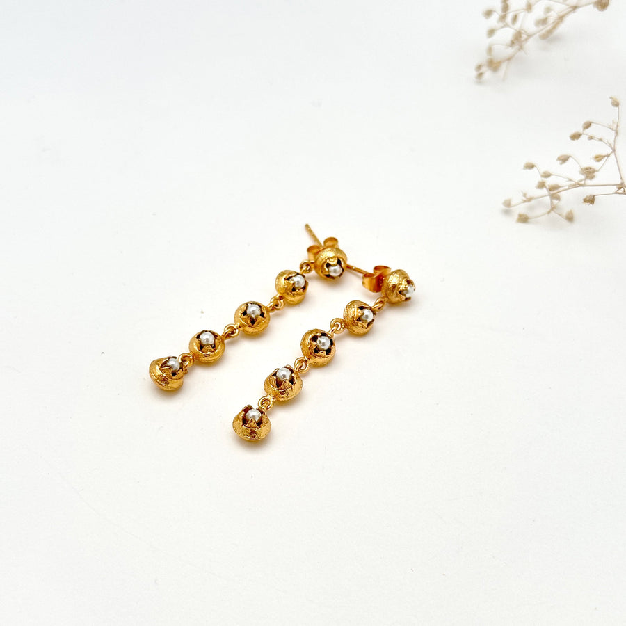 Flat lay close-up view showing the linked articulated pod construction and glass pearl details of the BEEJ dangle earrings.