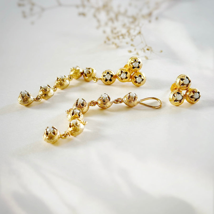 Soft studio flat lay displaying the 22K gold-plated BEEJ seedpod dangle earrings alongside matching cluster stud post earrings with glass pearls.
