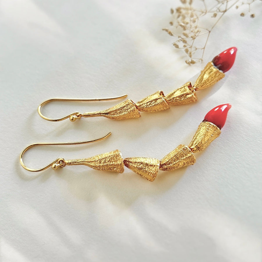 Side view flat lay of the MIRCHI gold pod chain dangle earrings with vibrant red borosilicate glass chili tips.