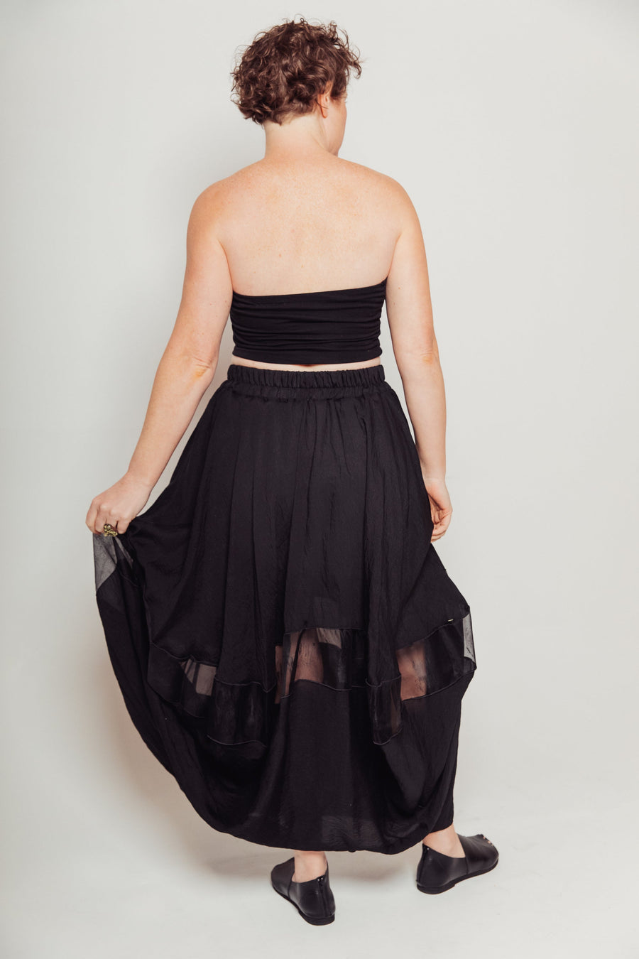 Back view of a model in a black bandeau top showcasing the gathered elastic waistband of the Silk & Modal Bellows Skirt.