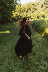 Rear perspective of a model walking through a grassy field wearing the volumetric black Bellows Skirt.