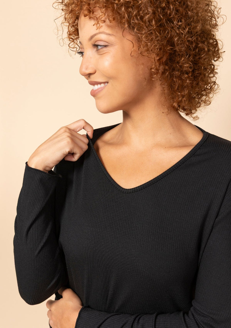 Close-up shot showing the V-neckline, merrow stitching, and ribbed modal fabric of the black Hedy Tee.