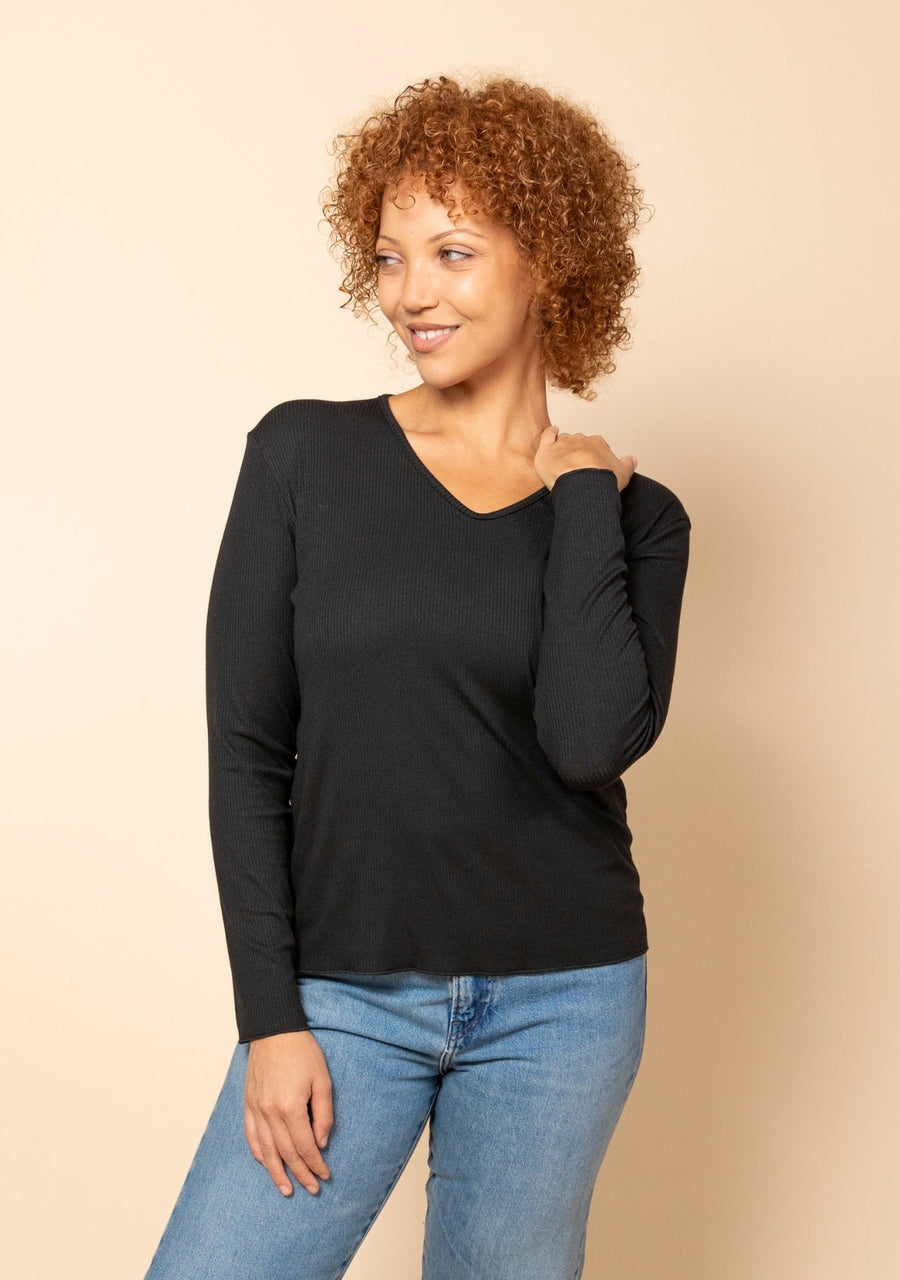 Model with curly hair posing hand on shoulder in the black Hedy Ribbed Modal V-Neck Long Sleeve Tee.