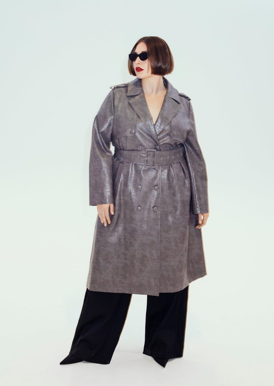 Plus-size model Beatrice wearing the grey textured vegan leather Hilary MacMillan Jodi Trench Coat with black trousers and sunglasses.   