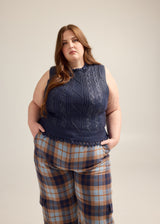 Plus-size model Rebecca wearing the Hilary MacMillan Navy Metallic Cable Knit Sweater Vest in size 3X paired with blue and brown plaid trousers.