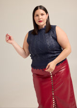 Model in red lipstick wearing the Hilary MacMillan Navy Metallic Cable Knit Sweater Vest with a red faux leather skirt.
