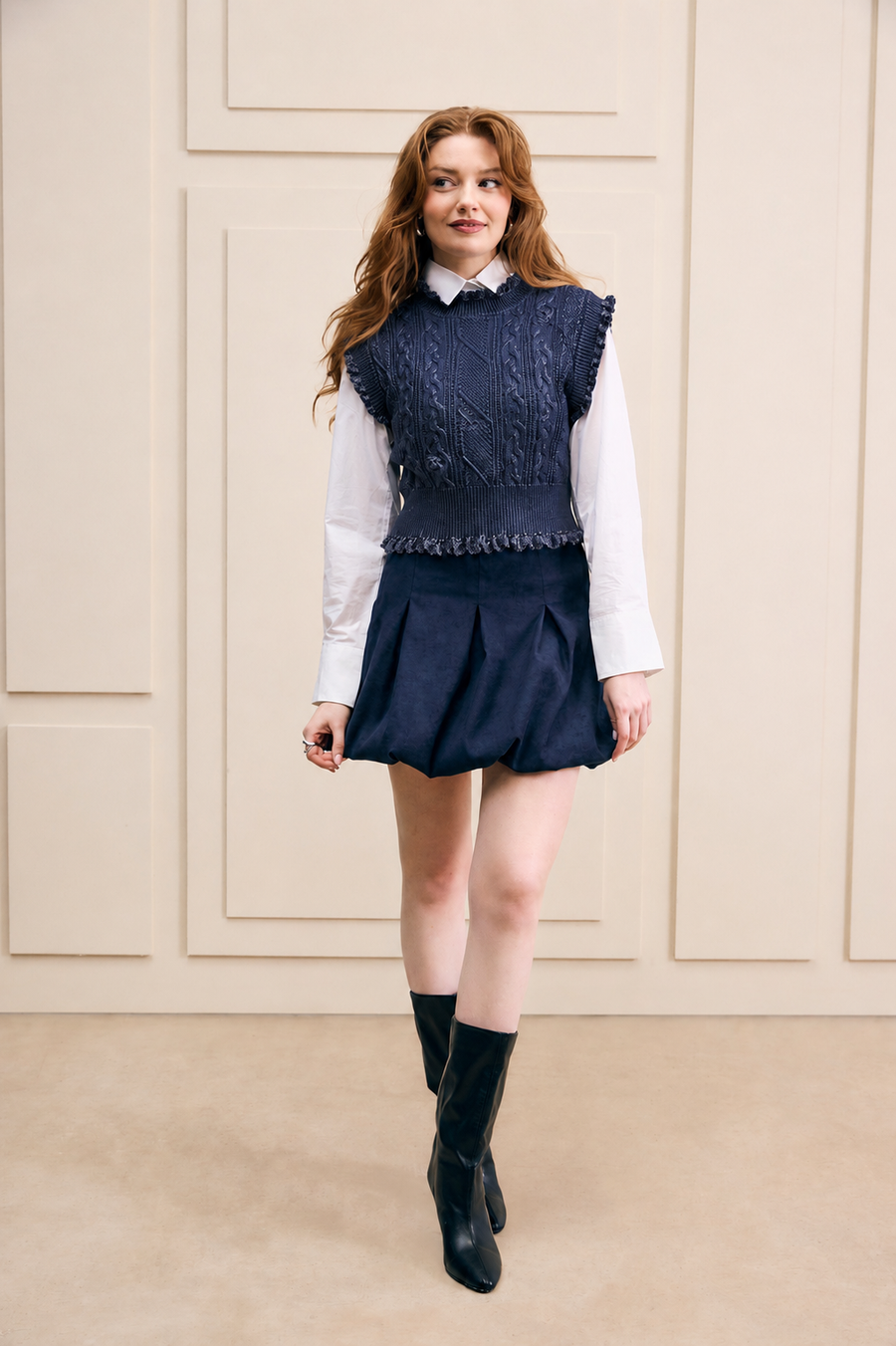Model Kiara wearing size S Hilary MacMillan Navy Metallic Sweater Vest layered over a white collared shirt with a navy bubble skirt and boots.