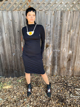 Full-length photo of a model with short dark hair wearing the black NOOWORKS Demi Dress styled with a statement geometric necklace and black star boots.