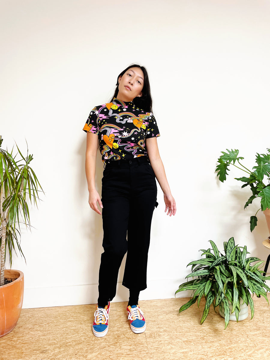 Model wearing Nooworks black twill painter pants styled with a printed mock-neck top and colorful sneakers.