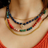 Model wearing a multi-strand necklace stack featuring the Phoebe Gemstone Necklace, lapis charm strand, and gold herringbone chain.