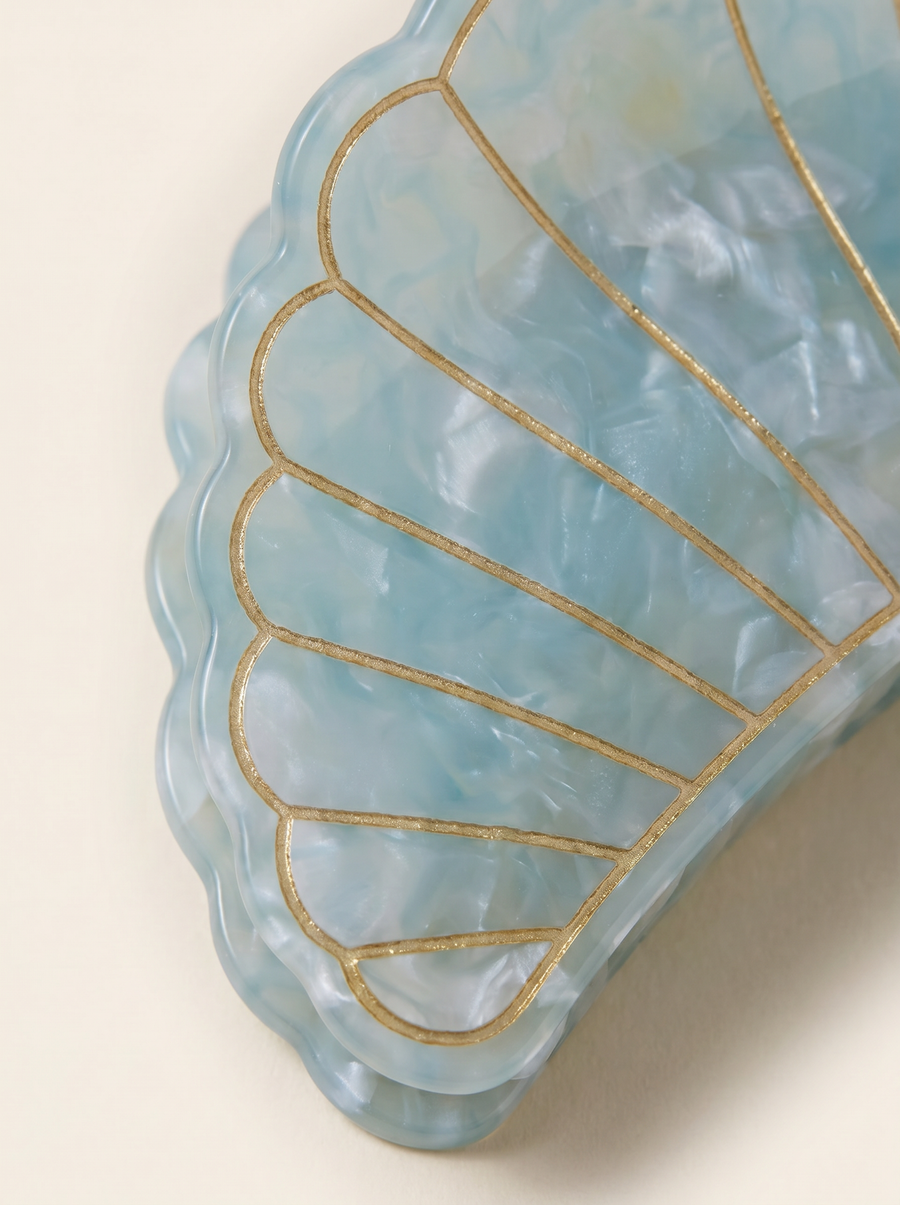 Flat lay view of the Village Thrive Shell Hair Clip in blue marbled recycled acetate, featuring decorative gold-lined shell ridge details.