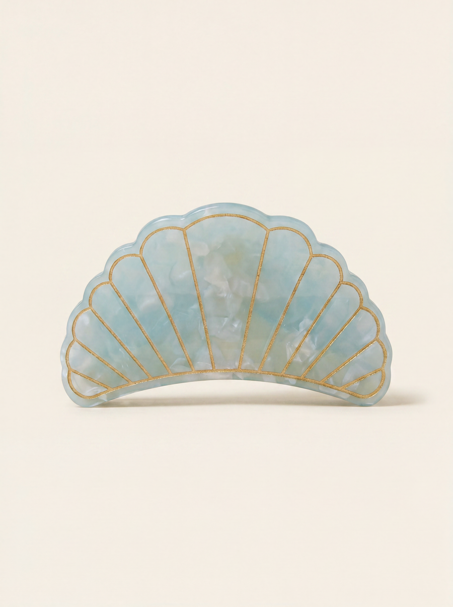 Flat lay view of the Village Thrive Shell Hair Clip in blue marbled recycled acetate, featuring decorative gold-lined shell ridge details.