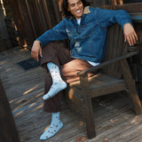 Lifestyle portrait of a woman wrapped in a checkered blanket sitting indoors wearing cozy baby blue puffin socks.