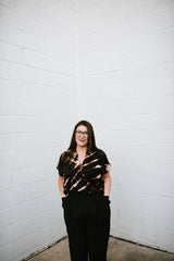 Full-length portrait of model in glasses wearing the Megan-Ilene Hand Dyed Silk Market Top styled with black pants.