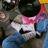 High-angle lifestyle photo of someone wearing Conscious Step guitar socks sitting near vinyl records and headphones.