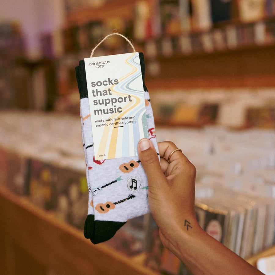 Person holding a packaged pair of Conscious Step Socks That Support Music in a record store.