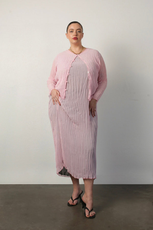 Full-length portrait of a model wearing the pink Maya Pleated Cardigan unbuttoned over the matching Jaya pleated dress.