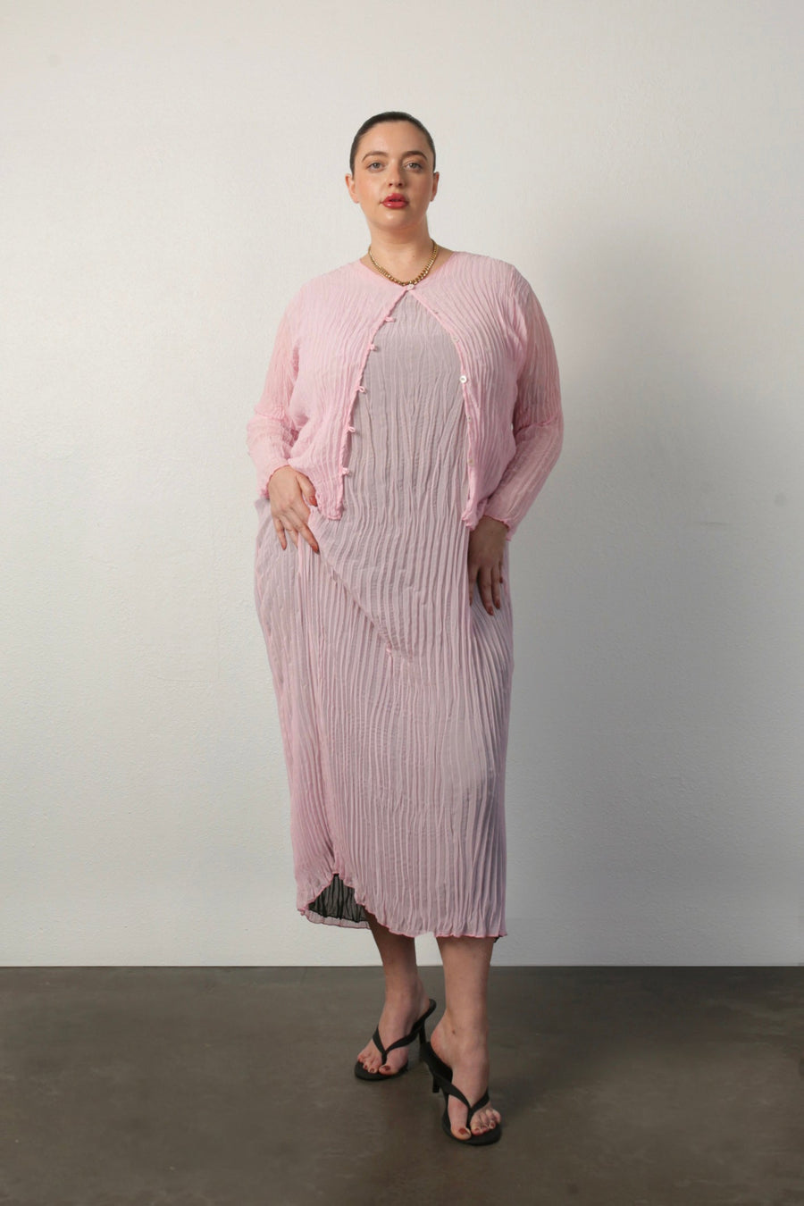 Full-length portrait of a model wearing the pink Maya Pleated Cardigan unbuttoned over the matching Jaya pleated dress.