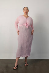 Studio portrait of a model wearing the Maya pink cardigan tied at the waist over a pleated midi dress.