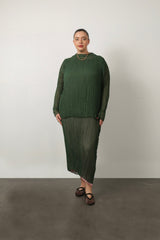 Full-length portrait of a model wearing the green Esme Pleated Funnel Neck Top styled with a matching green pleated midi skirt and gold chain necklace.