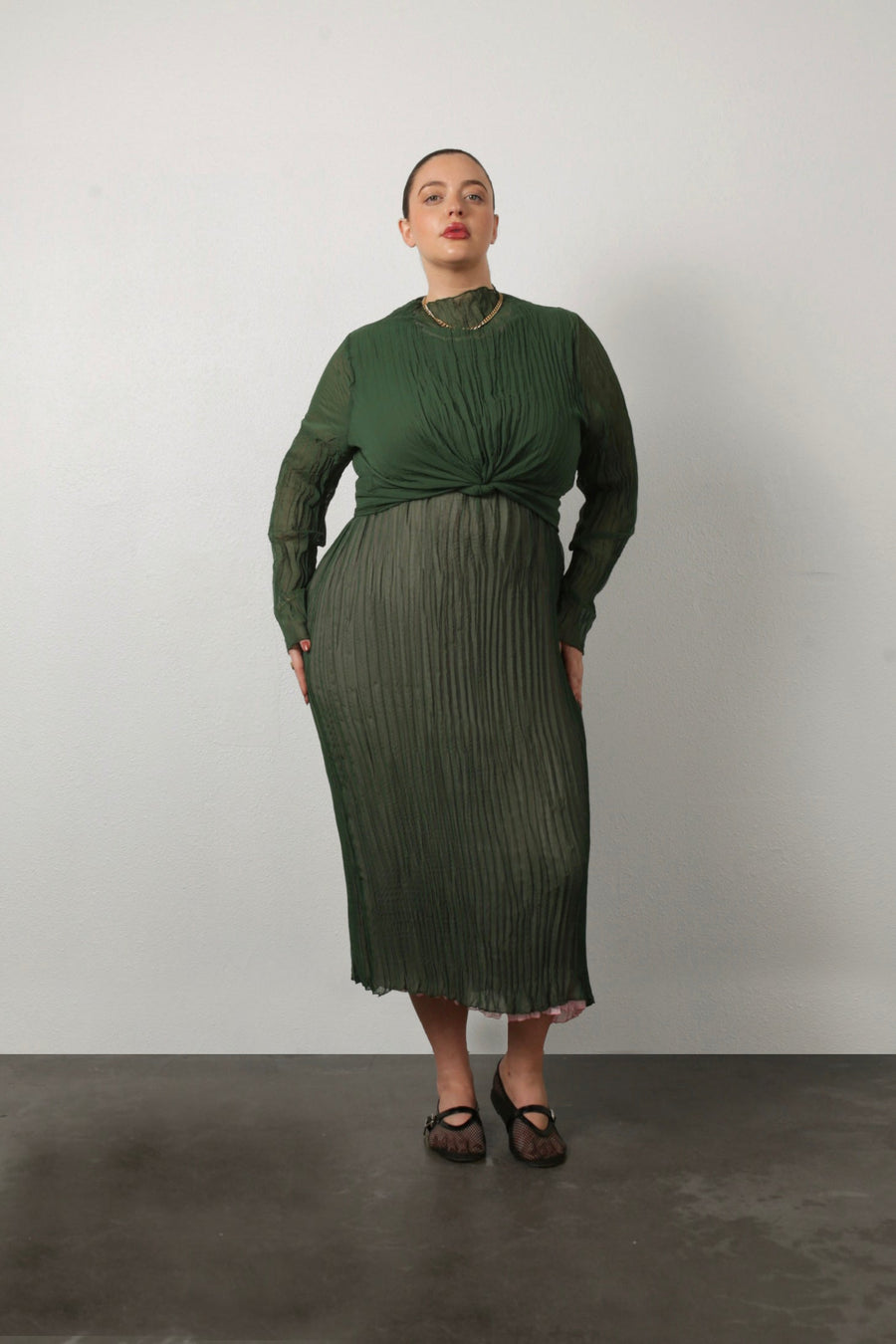 Studio photo of a model wearing the green Esme top tied into a front knot waist over a pleated midi dress.