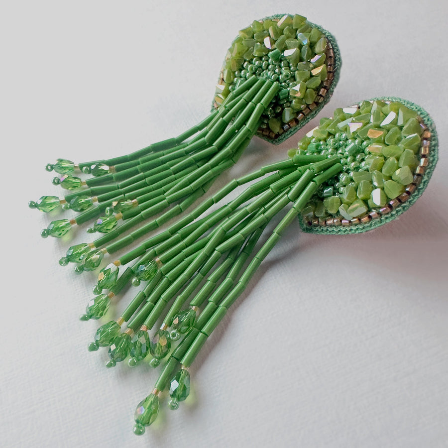 Front view of the green Fyoli Fyoli TORTULA Moss Hand Embroidered Earrings, featuring intricate glass beadwork on a velvet backing with a long, flowing beaded fringe against a white background.