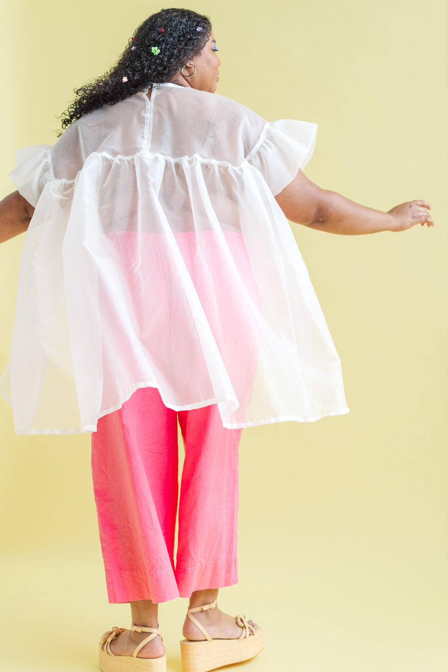 Model twirling from behind in the sheer white Nettle Studios Silk Organza Mini Mushroom Dress displaying its structured drape.