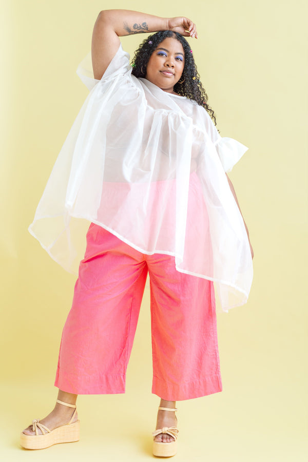 Model Angelina wearing the sheer white Nettle Studios Silk Organza Mini Mushroom Dress in OS+ layered over bright pink wide-leg trousers.