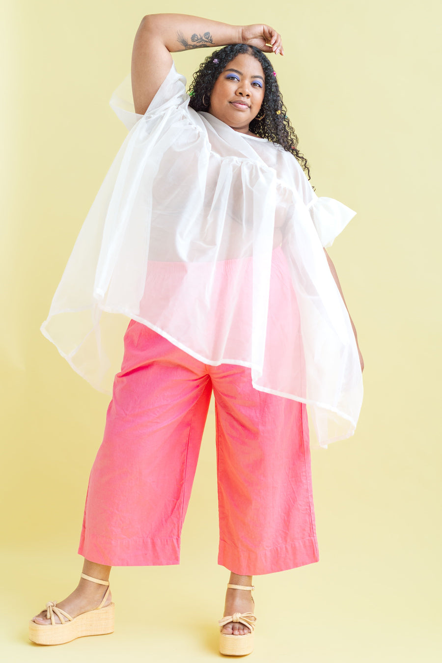 Model Angelina wearing the sheer white Nettle Studios Silk Organza Mini Mushroom Dress in OS+ layered over bright pink wide-leg trousers.