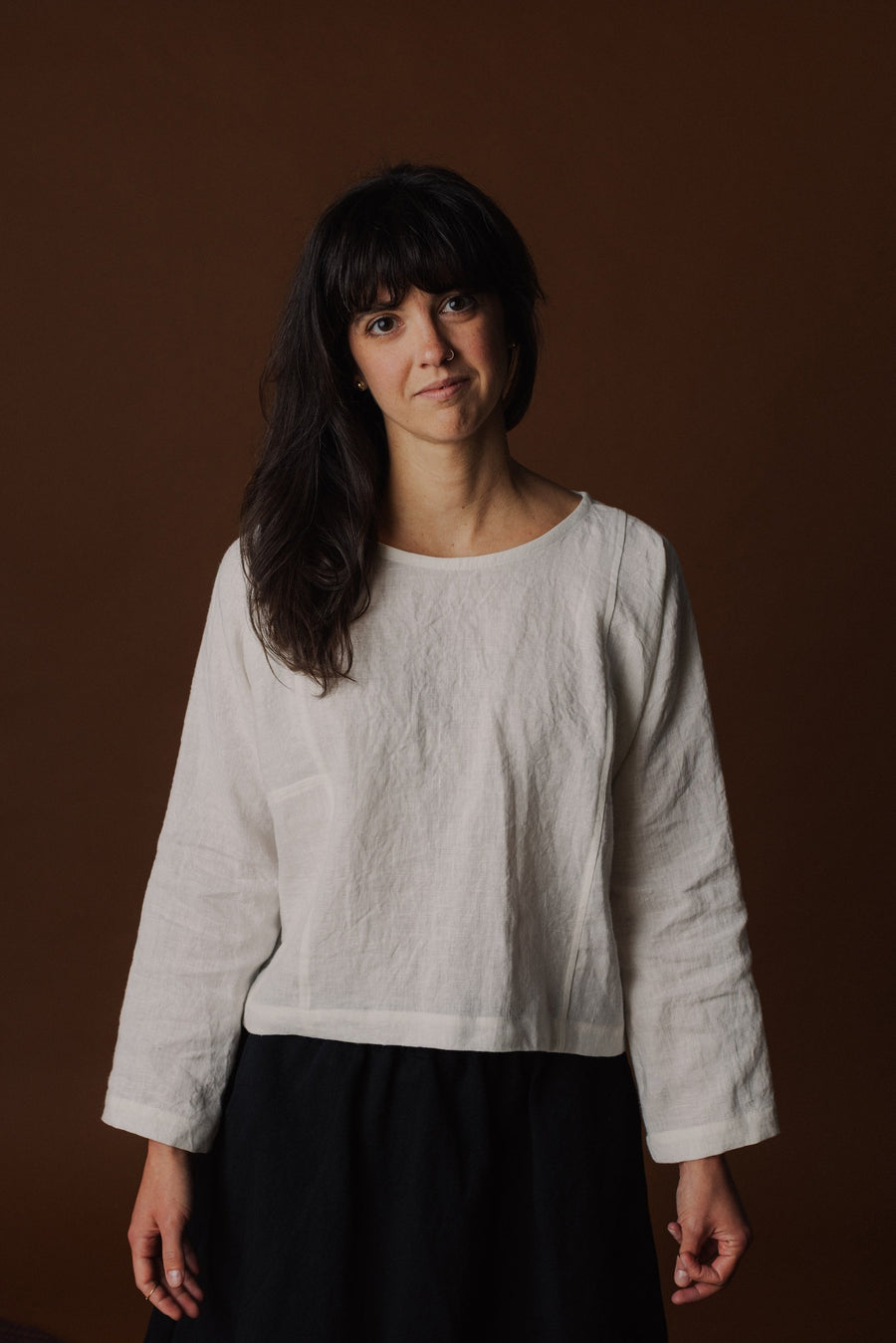 Studio portrait of Madison wearing the Pamut Apparel Molly Long Sleeve Top in White linen paired with a black skirt.   