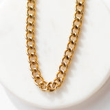 Close-up detail view of the 14k gold-plated stainless steel thick link chain of the Parker Necklace on a white marble display.