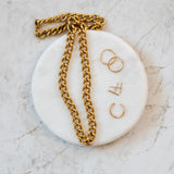 Overhead flat lay of the Parker gold link necklace styled alongside gold hoop earrings and delicate jewelry on a round marble plate.