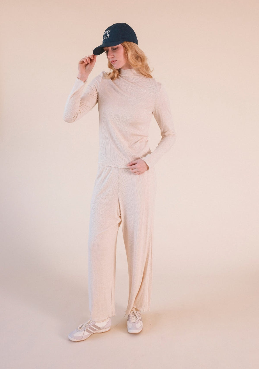 Full-length studio portrait of a model wearing the Heather Almond Poplinen Hedy Ribbed Modal Lounge Pant set with a navy cap.