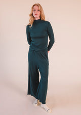 Full-length studio portrait of a model wearing the dark green Poplinen Hedy Ribbed Modal Lounge Pant matching set.